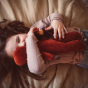 A child holding the Senger Large Poppy Flower doll and a small Moss Violet doll in the arms whilst lying down on a beige cloth