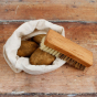 A Slice of Green vegetable scrubbing brush on top of an open bag of potatoes on a wooden worktop
