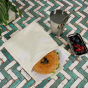 Stuffed bagel inside A Slice of Green large food baggie on some green and white tiles, next to a pot of fruit and steel cup