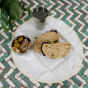 A Slice of Green organic cotton food wrap on some green and white tiles with a sandwich, snack pot and steel cup