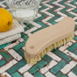 A Slice of Green beech wood scrubbing brush on a green and white tiled floor next to a lemon and pot of salt