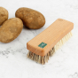 A Slice of Green plastic-free wooden vegetable brush on a white background next to a pile of potatoes