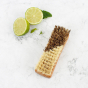 A Slice of Green plastic-free vegetable brush upturned on a white background next to a sliced lime, showing the plant-based bristles