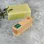 A Slice of Green plastic-free wooden nail brush on a grey background next to a bar of soap