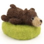 A fully made The Makerss - Amiguwoolli Tiny Chicken Mini Needle Felt Figure. The bear has a brown body, legs, tail and ears. Stick in eyes, a light brown snout and a black nose an mouth, and is laid down on a light green felted base