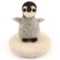 A made The Makerss - Amiguwoolli Tiny Penguin Mini Needle Felt Figure. The penguin is made from grey felting wool, with black feet and head, a black stick in eye and white face, on a felted cream base
