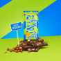 Tony's Chocolonely Dark Creamy Hazelnut Crunch Bars broken up and stacked up with a wrapped bar on top pictured on a blue and green coloured background