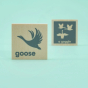 Two wooden Uncle Goose collective noun toy blocks showing a goose an a gaggle of geese on a green background