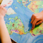 Close up of childrens hands pointing at countries on the Waldorf family plastic-free wooden world map board
