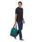 Man walking on a white background carrying the Patagonia ultralight black hole tote pack in the borealis green colour 