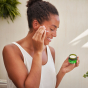 An image of a person applying the Weleda Skin Food Nourishing Day Face Cream to their cheeks, they are holding the pot in their hands 