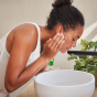 A person leaning over a bathroom sink rinsing the Weleda Skin Food Nourishing Cleansing Balm to their face 
