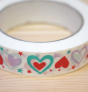 The Babipur Love Heart Paper Tape is a white self-adhesive paper tape with a gorgeous love heart and stars print in red, turquoise and purple on a wooden table.