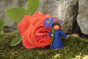Close up of a handmade felt cornflower fairy figure stood in front of a large red flower