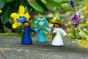 3 collectable Ambrosius summer fairy figures stood on a wooden log in front of some purple and yellow flowers