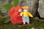 Close up of a handmade felt rainbow child figure stood in front of a large red flower