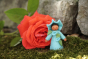 Close up of a handmade felt blue morning glory fairy figure stood in front of a large red flower