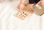 Close up of childs hand playing with the eco-friendly wooden Babai tic tac toe toy on a white bed sheet