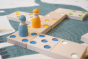 Close up of two wooden peg doll figures on top of the Bajo kids wooden XXL dominos game on a blue and white carpet