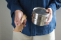 person holding the Bambu Bamboo Utensil Travel Set with Cork Fabric Pouch with a metal food tin