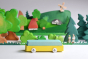Bumbu waldorf car toy on a white table in front of a green wooden landscape scene 