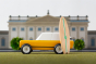Candylab cotswold gold toy car on a green background with a miniature wooden surfboard in front of a palace model