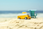 Close up of a wooden Candylab vw campervan toy on a sandy beach in front of a blue sky