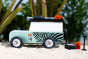 Side of the candylab wooden zebra drifter vehicle toy on some sand in front of a green plant