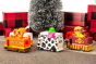6 wooden Candylab toy trucks lined up on a brown carpet in front of a Christmas tree and some red presents
