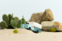 Close up of the Candylab wooden SUV toy on some sand in front of a stack of rocks and a miniature cactus