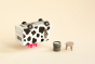 Candylab toy milk truck upside down, balancing on its pink udders, on a beige background next to a miniature stool and bucket of milk