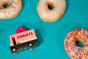 Candylab donut van, 60s style americana wooden van on a teal background with 3 iced ring donuts