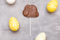 Cocoa Loco eco-friendly 26g chocolate bunny lolly on a grey background next to some yellow and white easter eggs