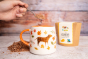 Close up of hand holding some Cocoa Loco organic hot chocolate flakes on a spoon above a white mug with a dog painting on the front