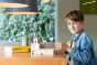 Young boy sat at a wooden table playing with the plastic-free Cuboro wooden marble run standard building kit