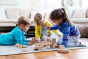 3 children sat in a circle playing with the Cuboro plastic-free marble run building kit on a blue carpet