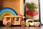 Debresk wooden bus and oldtimer vehicles on a wooden floor in front of a Grimms wooden rainbow and drei blatter radish puzzle