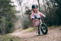 Young girl stood on a woodland path, riding an Early rider charger 12 inch balance bike