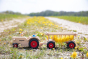 Fagus handmade wooden tractor and hay cart toy on a grass field carrying some dandelions