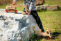 Child playing with the Fagus handmade wooden truck and excavator toy on a large white rock