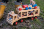 Close up of childs hand holding the Fagus large wooden car transporter lorry toy on some wet grass and autumn leaves
