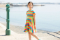 Child wearing the Frugi Rainbow Stripe Spring Skater Dress with a seaside view behind them