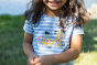 Close up of a child wearing the Frugi Tide blue Breton striped Bicycle Elise Applique T-Shirt showing the bicycle applique 