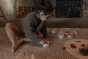 Girl playing on the floor with 6 small grey pots, filled with red Grapat Mandala Flower Petals.