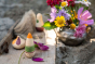 Close up of the Grapat plastic-free ooh lala toy figures on a wooden plank next to a jar of purple and yellow flowers