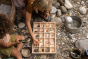 Children laying out pieces of the Grapat Wonders wooden toy set in a wooden box next to small rocks and shells