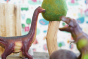 Close up of a green rubber toys sustainable dinosaur next to a papoose wooden tree toy
