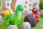 Close up of the green rubber toys eco-friendly mini dinosaurs stood on some green felt behind a papoose felt rock toy
