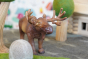 Close up of a green rubber toys moose figure on some grey felt in front of a papoose wooden tree toy