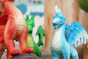 Close up of a green rubber toys blue ice dragon in front of a papoose wooden tree toy
